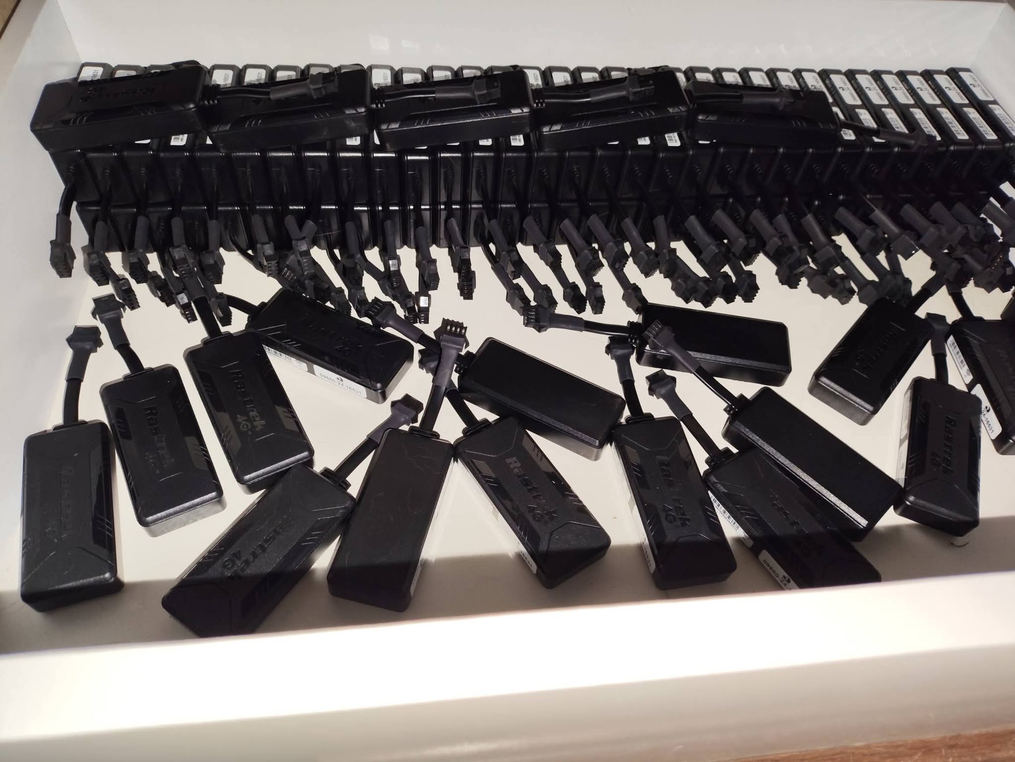 vários dispositivos rastreadores pretos X3 ELWIRE com cabos e conectores organizados em fileiras sobre uma sup
